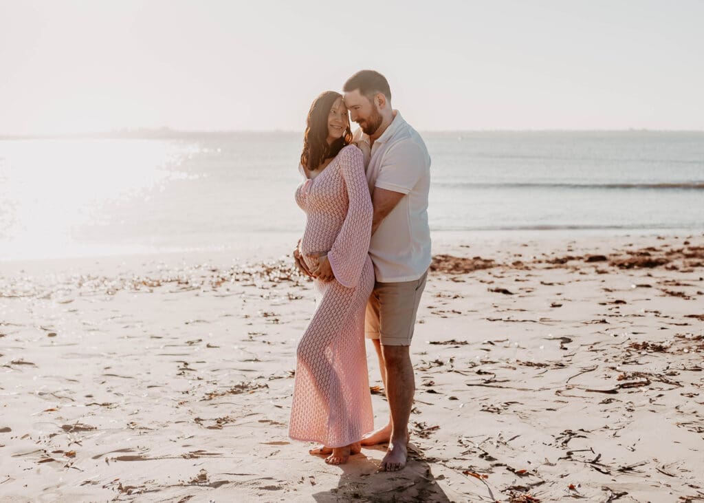 Couple embracing a bsby bump on the beach at sunset