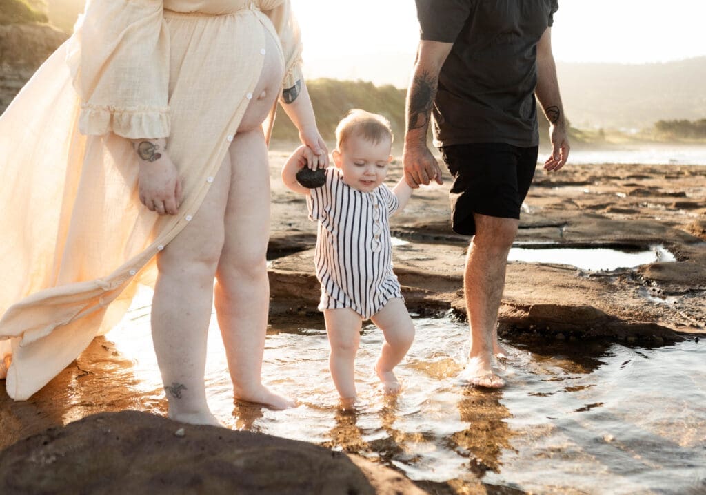 Family holding hands walking along the rocks at the beach at sunset